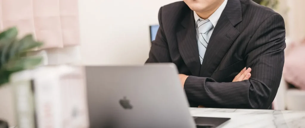 パソコンの前で腕を組み、社内のセキュリティリスクや情報漏洩対策について思案するスーツ姿の男性